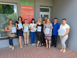 Wspólne zdjęcie grupy szkoleniowej z certyfikatami przed budynkiem.